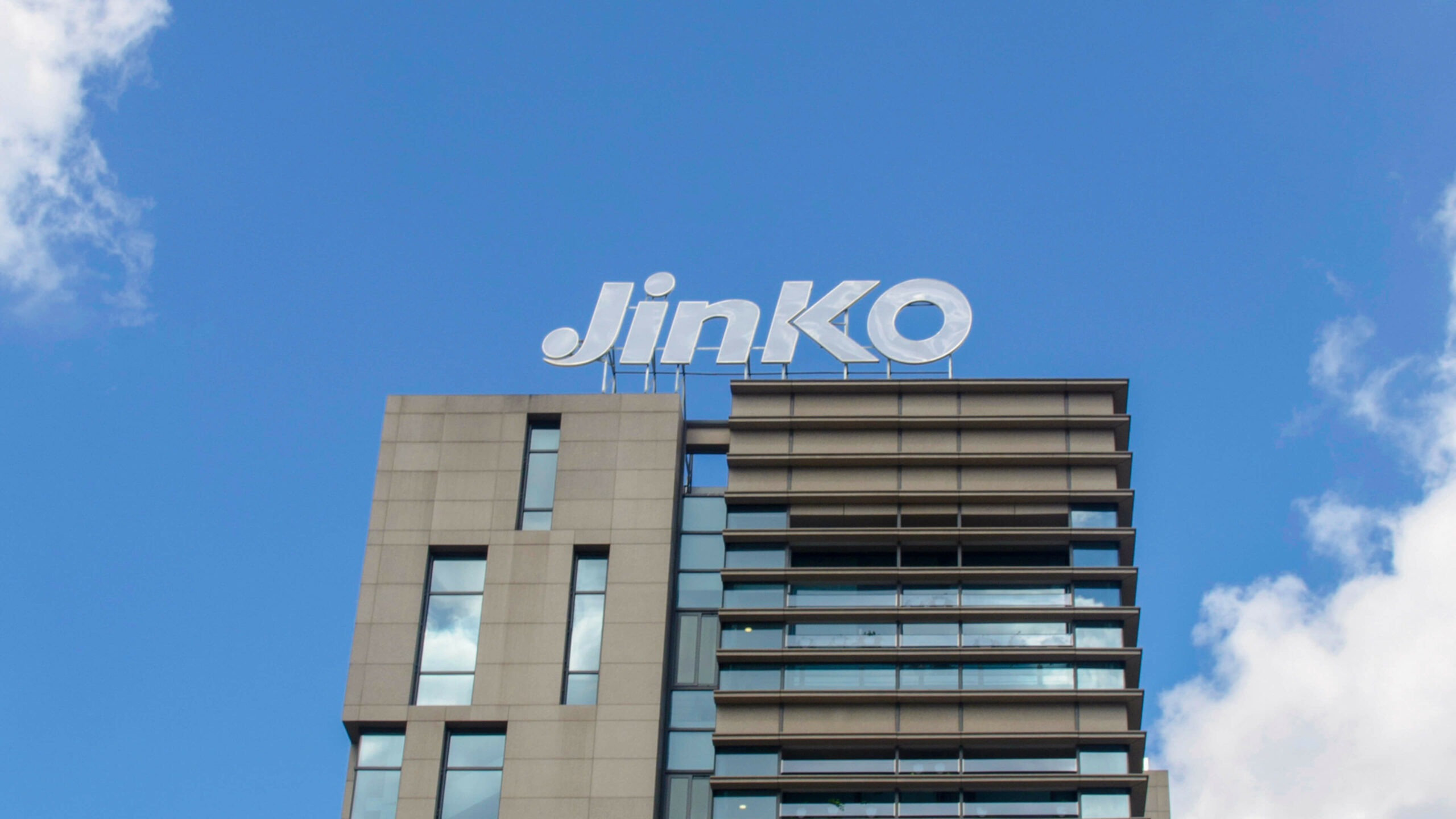 The Jinko Solar logo is positioned on the top of a modern office building against a blue sky